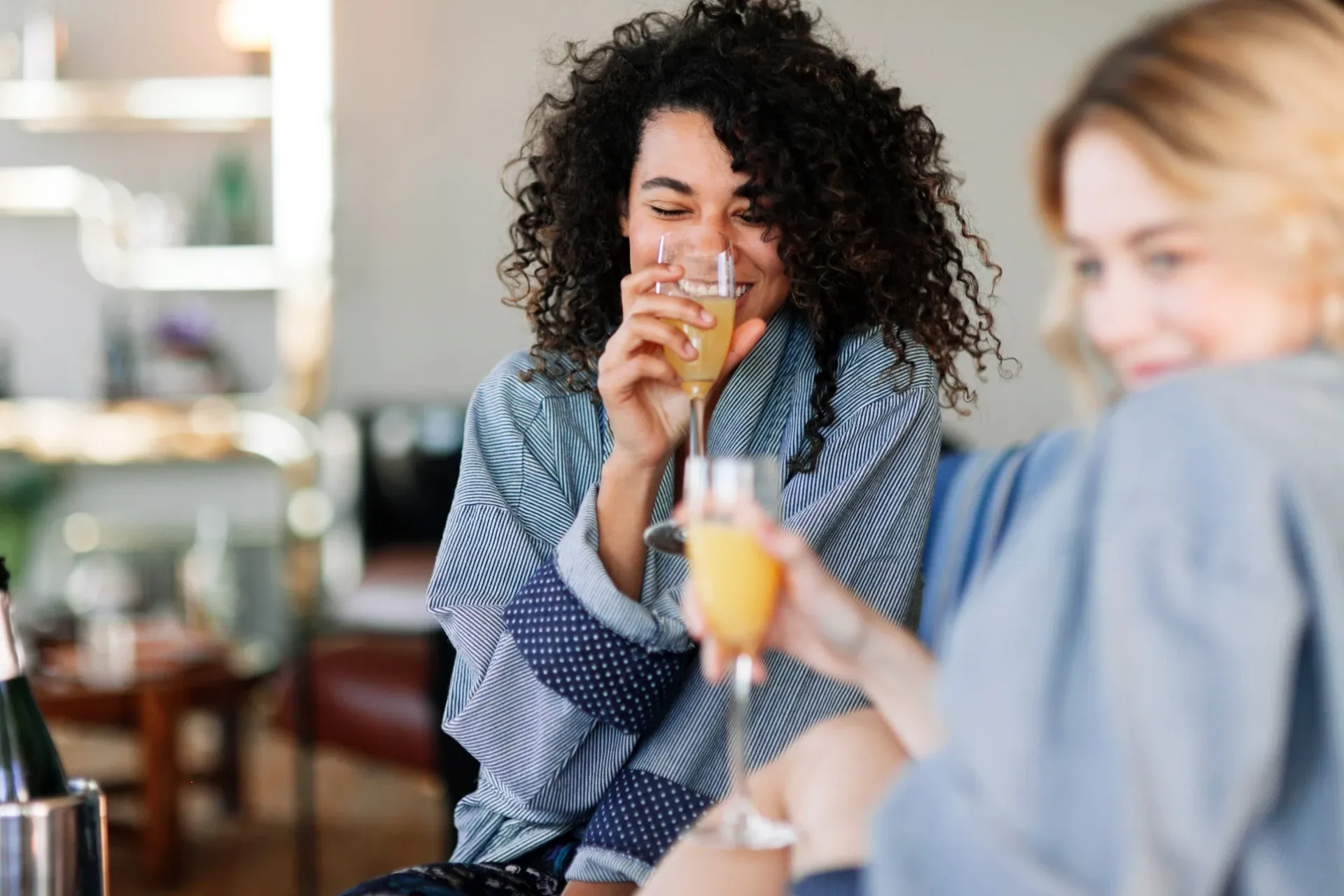 A young woman laughs with a friend over mimosas in the brightly lit clubroom