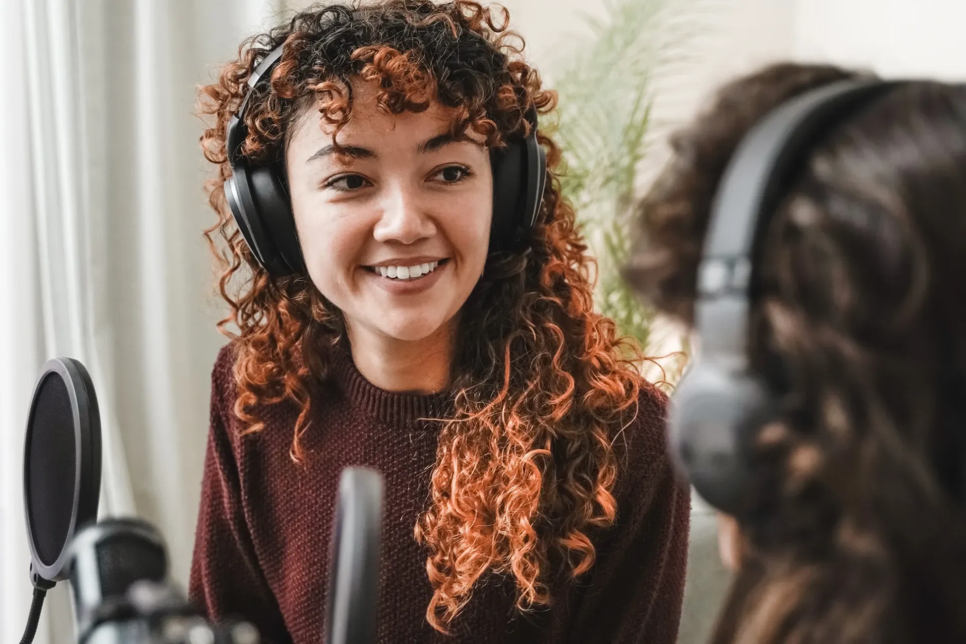 A smiling young woman records a podcast in a creative, modern workspace